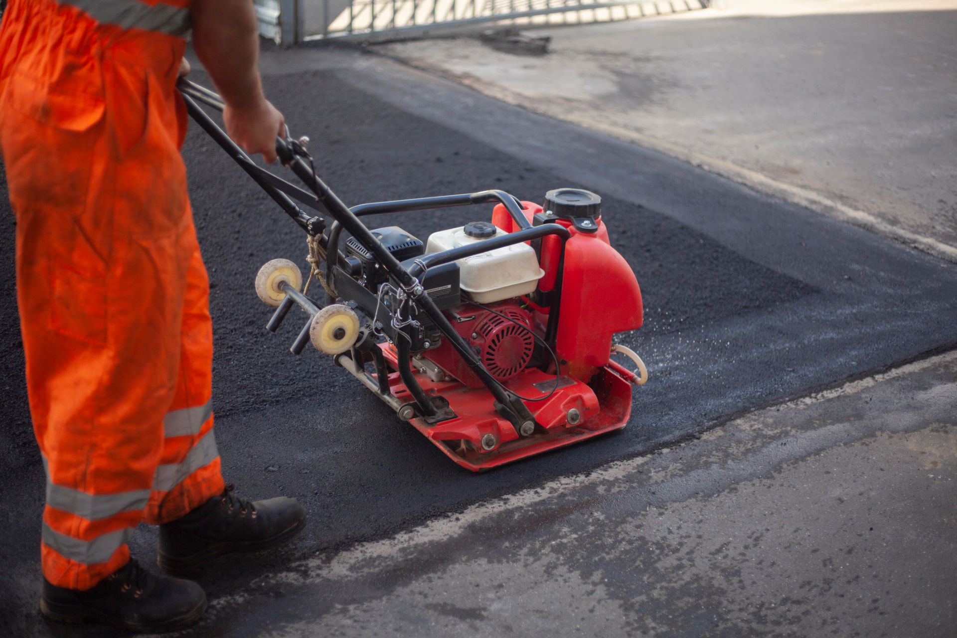 Worker compacting an asphalt patch with a red plate compactor