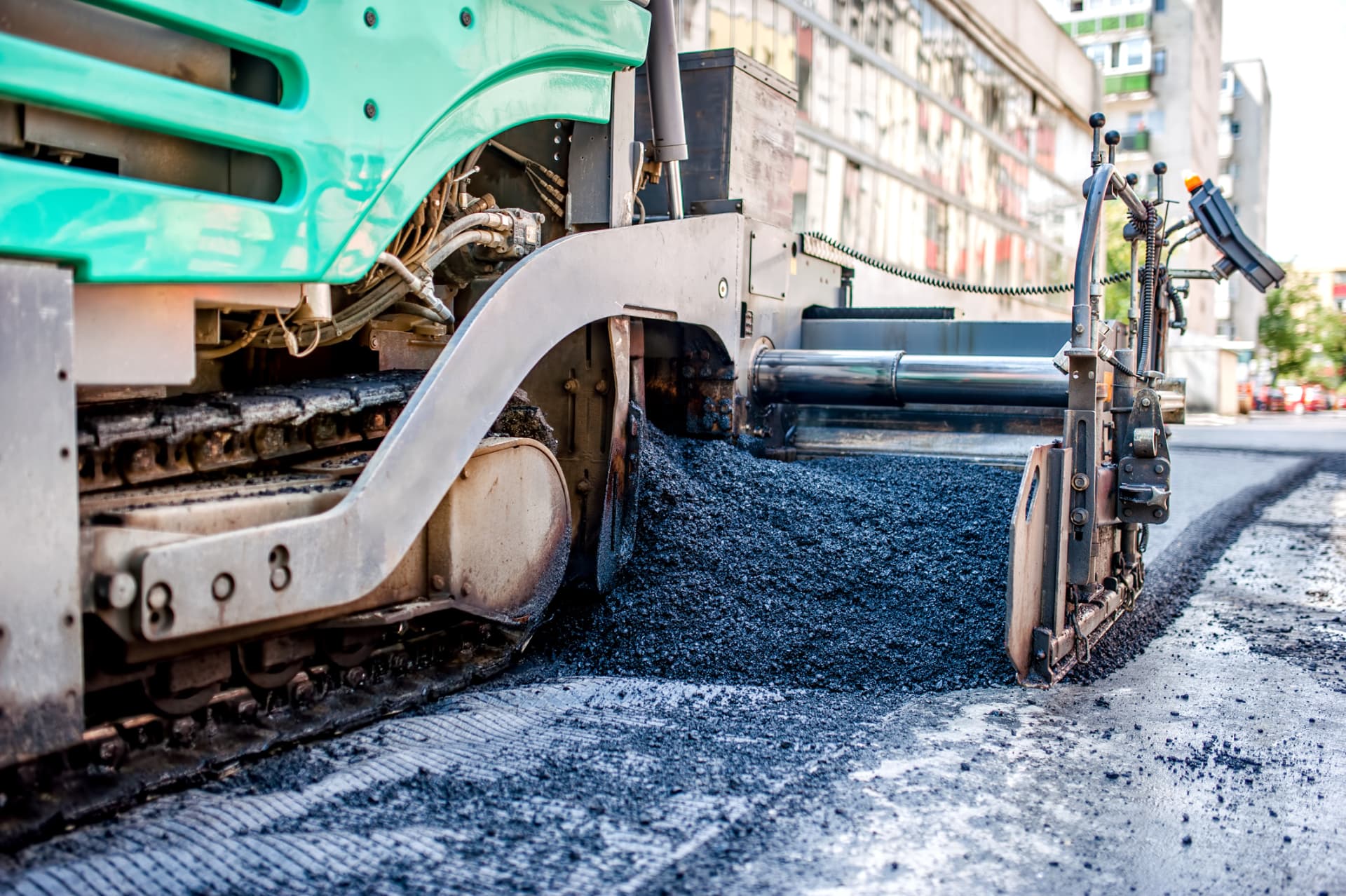 Asphalt paver screed laying a fresh mat of hot mix along a residential street